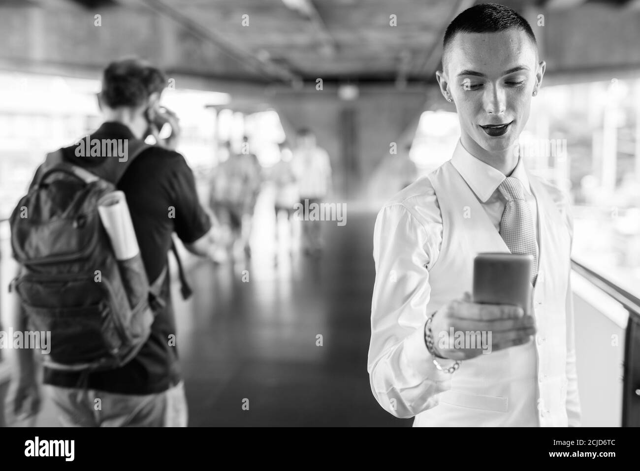 Joyeux jeune homme d'affaires androgyne beau utilisant le téléphone dans la ville Banque D'Images