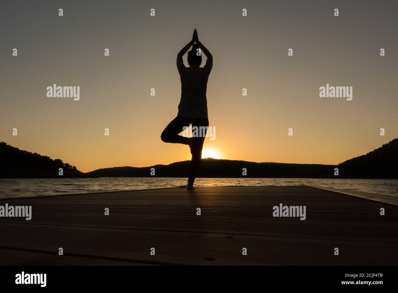 une jeune fille faisant du yoga pose sur un quai au coucher du soleil. Posture de l'arbre Banque D'Images