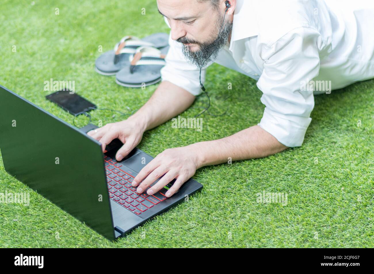 un homme de taille basse avec une barbe sur le sol à la maison tout en travaillant sur son ordinateur portable Banque D'Images