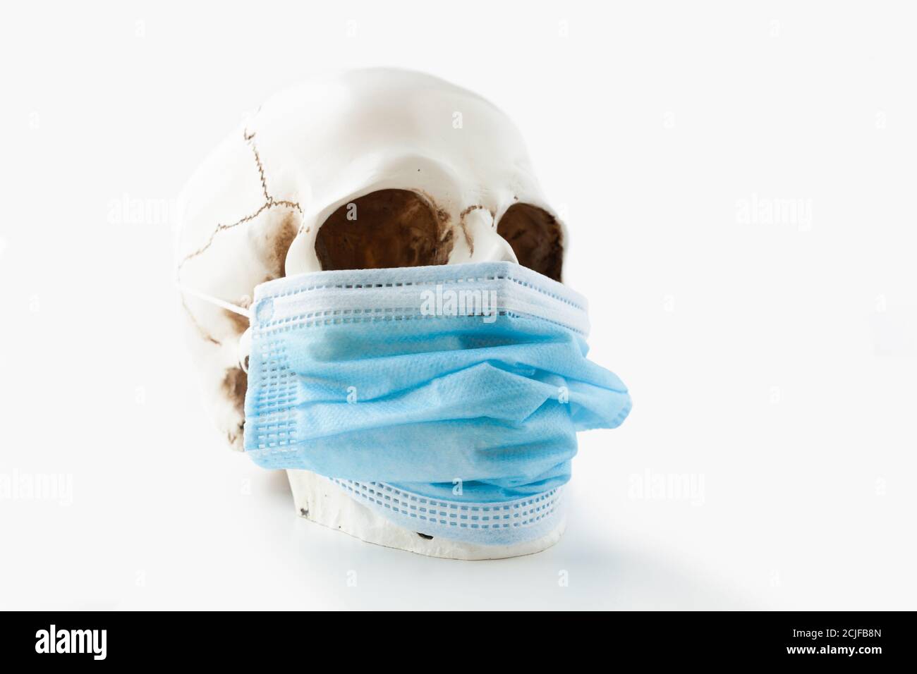 Crâne humain portant un masque chirurgical bleu sur fond blanc, vue latérale Banque D'Images