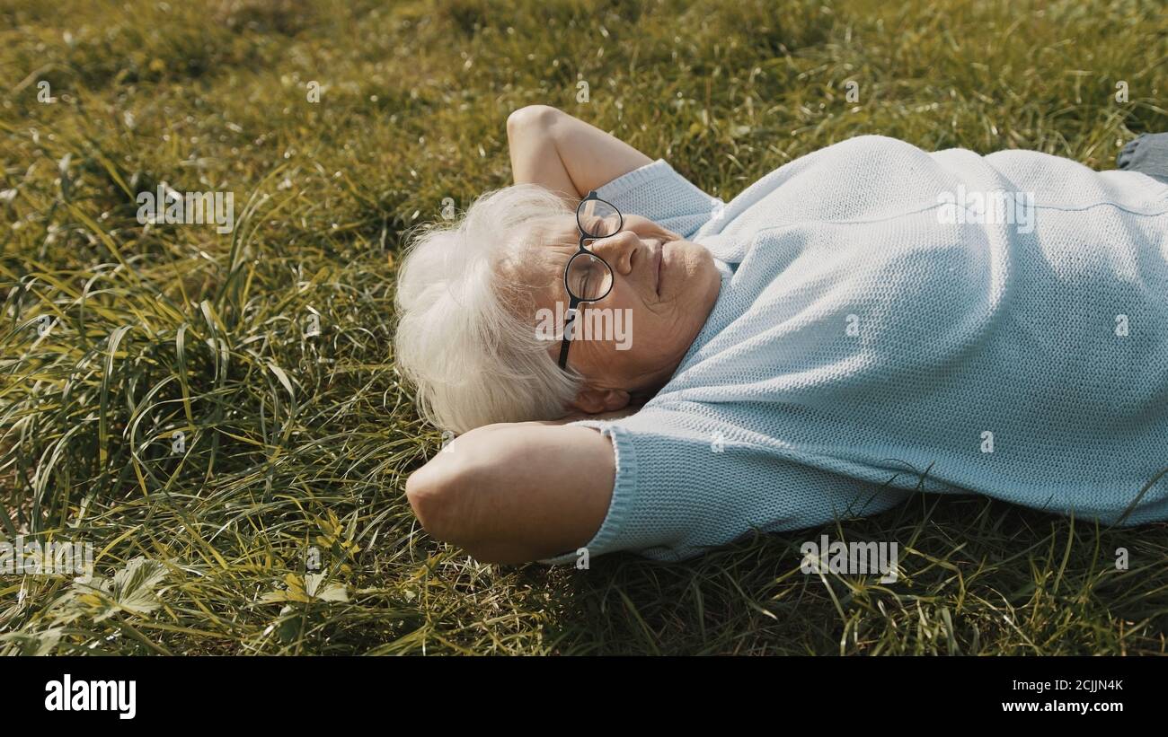 Grand-mère frais couché sur l'herbe avec les mains sous sa tête. Repos dans la nature. Photo de haute qualité Banque D'Images