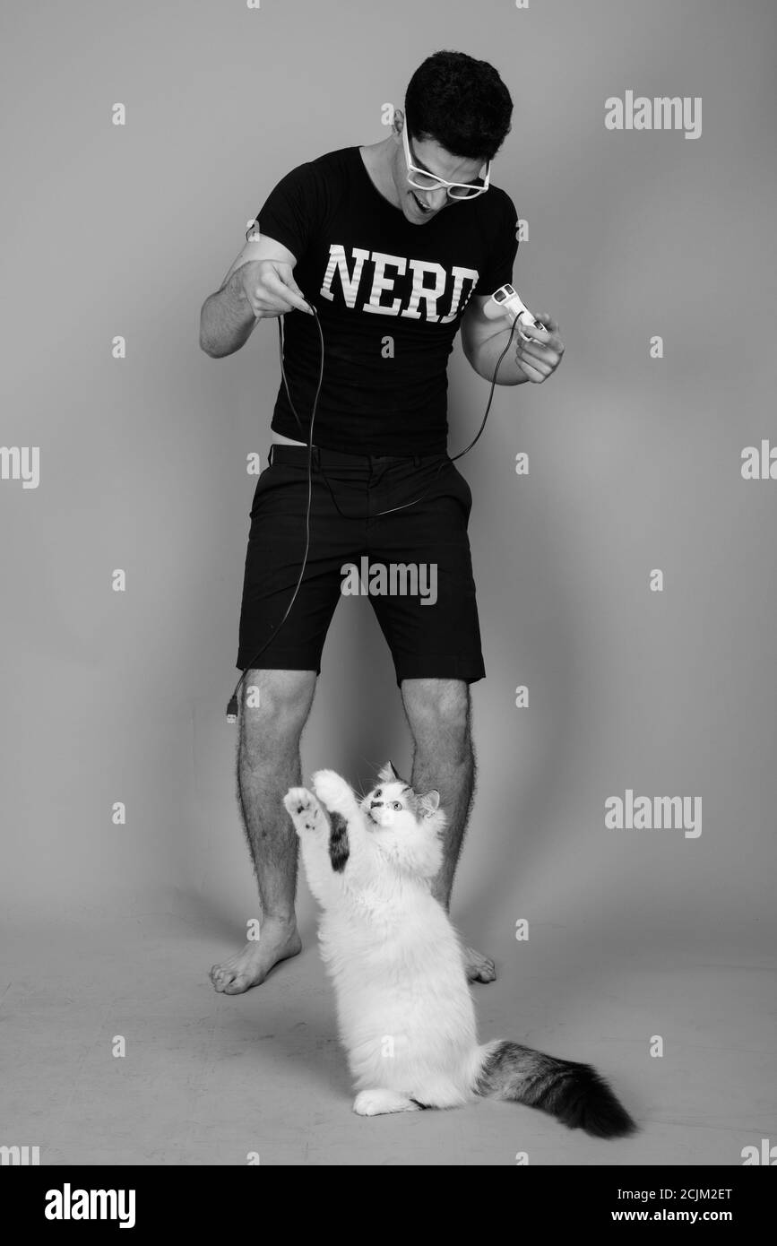 Portrait du jeune Perse nerd heureux homme jouant des jeux avec cat Banque D'Images Portrait du jeune Perse nerd heureux homme jouant des jeux avec cat Banque D'Images