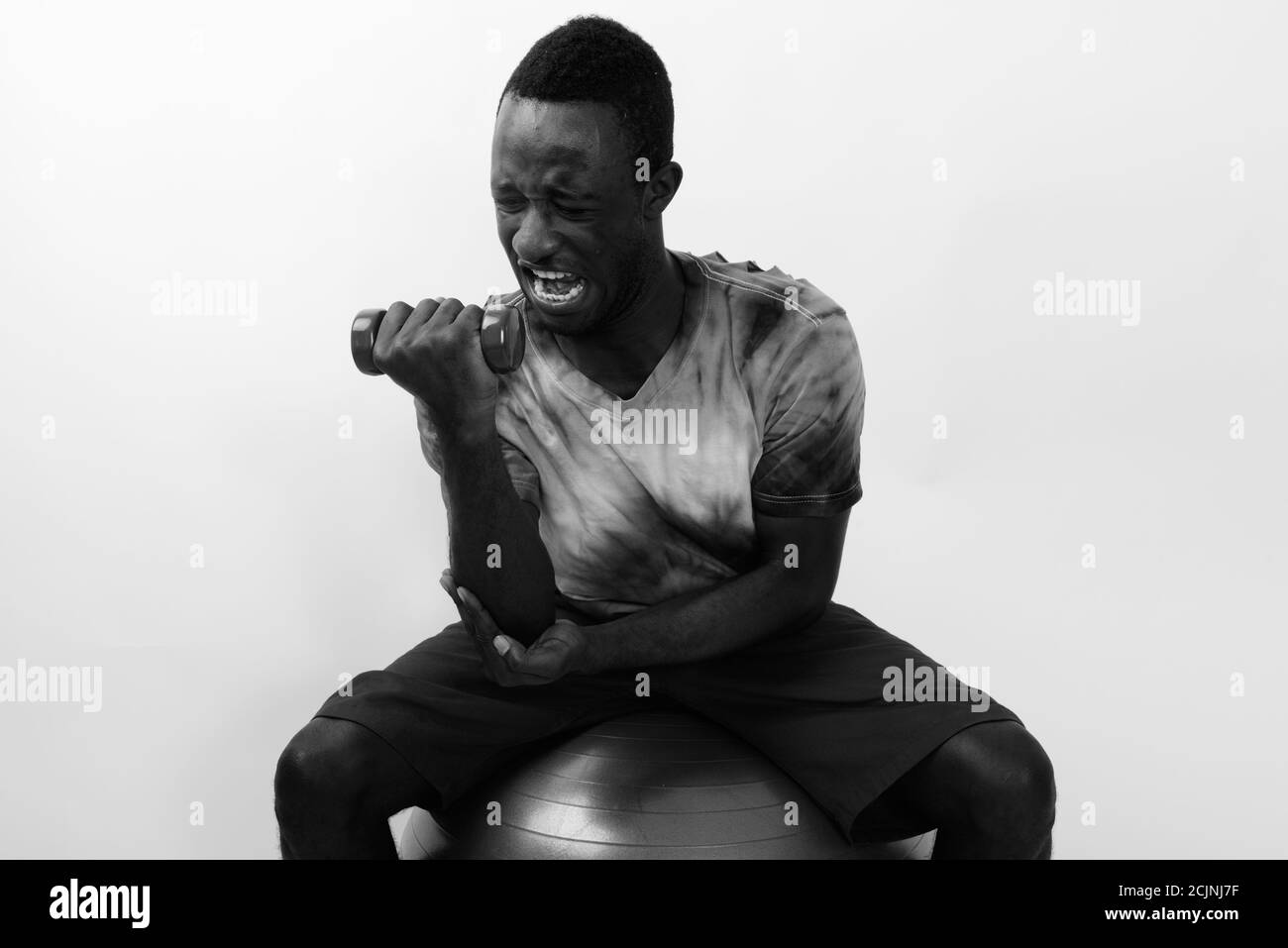 Jeune homme de fitness africain assis sur le ballon d'exercice tout en faisant boucle bicep avec haltère légère Banque D'Images