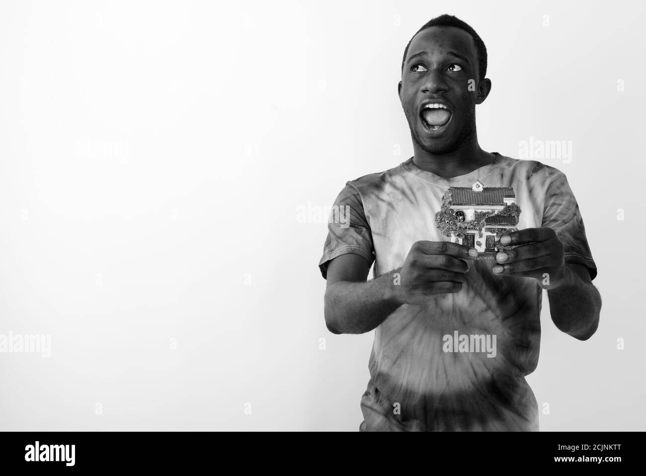 Photo en studio d'un jeune homme africain noir heureux tout en pensant et tenant la maison miniature sur fond blanc Banque D'Images