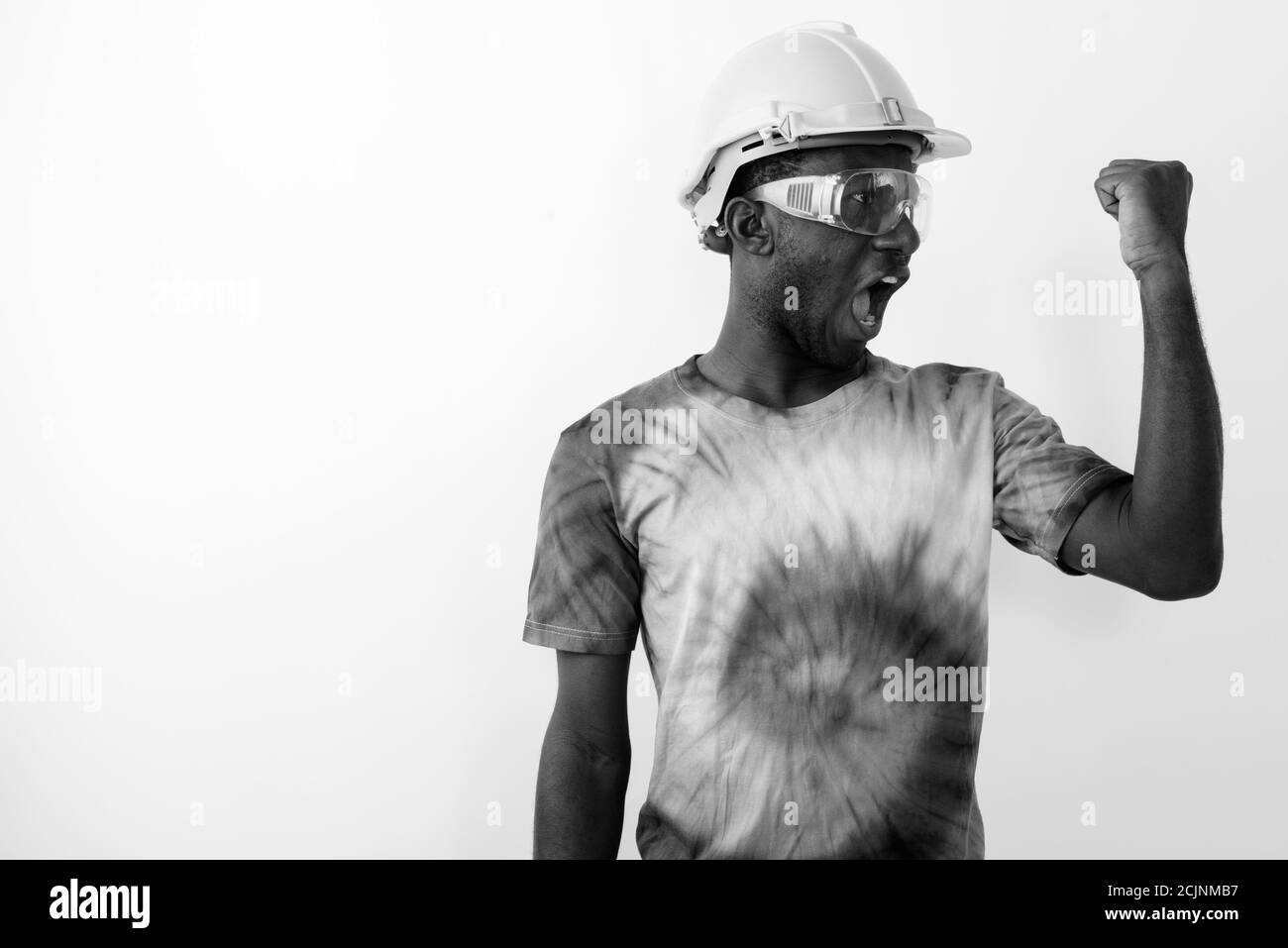 Jeune homme de construction africain noir portant un casque et lunettes de sécurité tout en fléchissant son biceps Banque D'Images