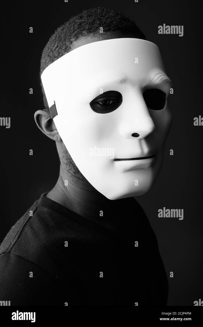 Studio shot of young black African man wearing mask in dark room Banque D'Images