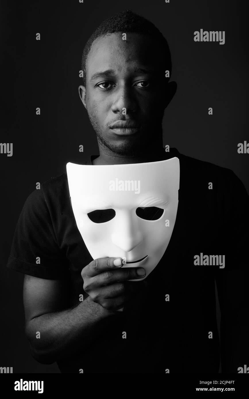 Studio shot of young black African man in dark room holding mask Banque D'Images