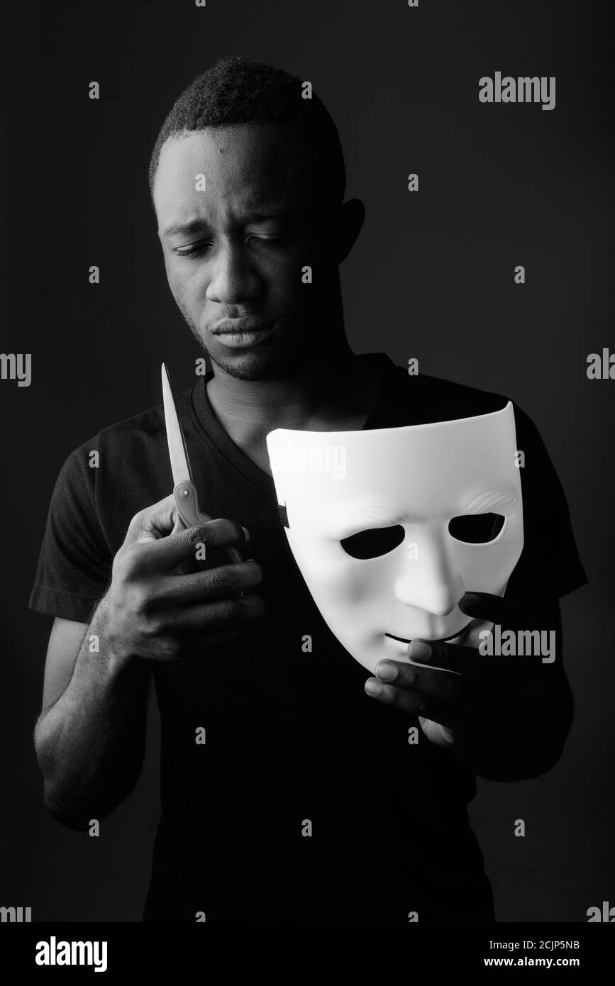 Studio de photo de jeune homme africain noir tenant le masque et ciseaux dans la pièce sombre Banque D'Images