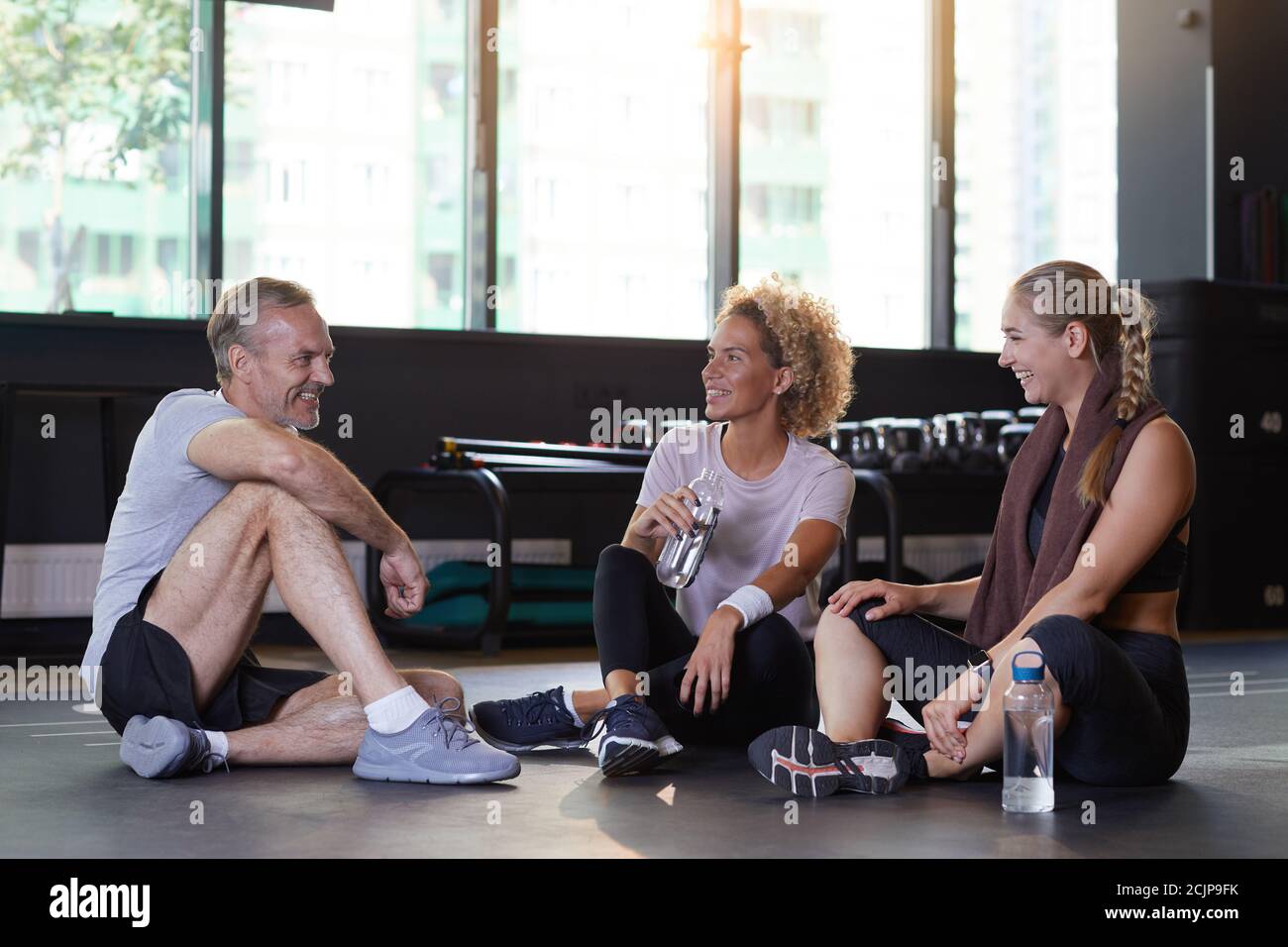 Groupe de personnes assis sur le plancher de l'eau potable et discuter entre eux après un entraînement sportif en salle de gym Banque D'Images