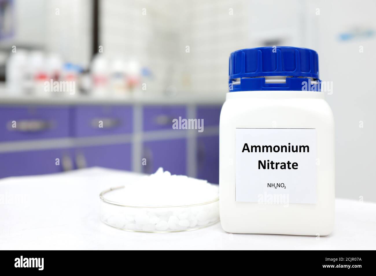 Mise au point sélective d'une bouteille de nitrate d'ammonium dans une bouteille en plastique à côté d'une boîte de Petri avec des pastilles blanches à l'intérieur d'un fond de laboratoire. Banque D'Images