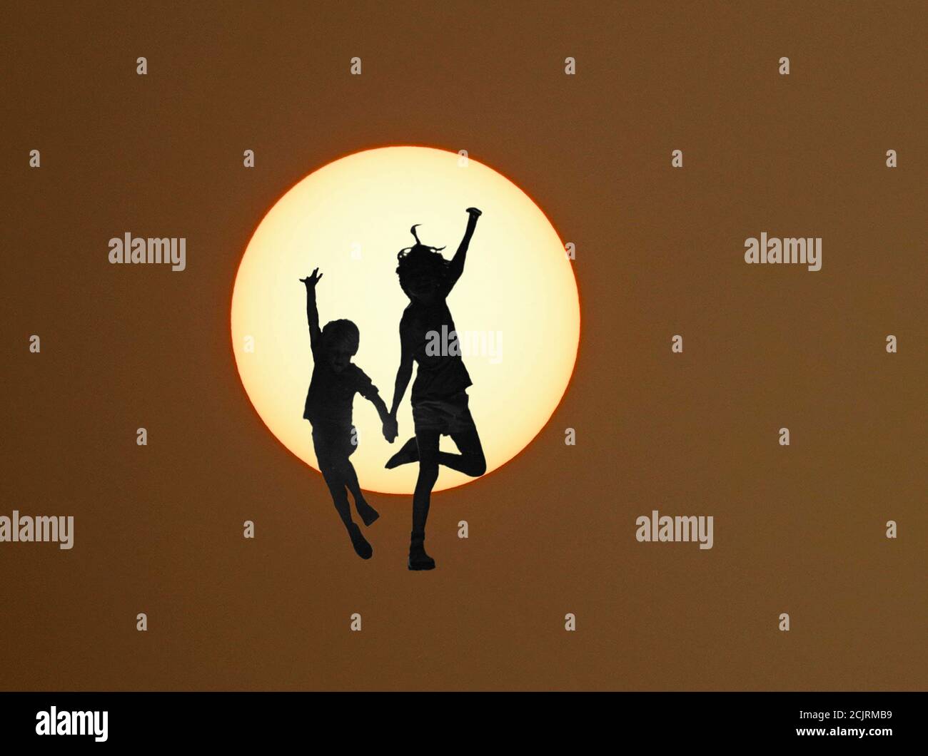 Silhouette d'un frère et d'une sœur dansant sous le soleil. Banque D'Images