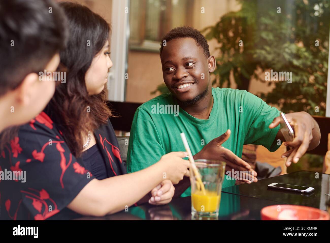 Groupe multiracial d'amis ayant un café ensemble. Un jeune homme noir explique quelque chose à sa petite amie entourée d'amis. Banque D'Images
