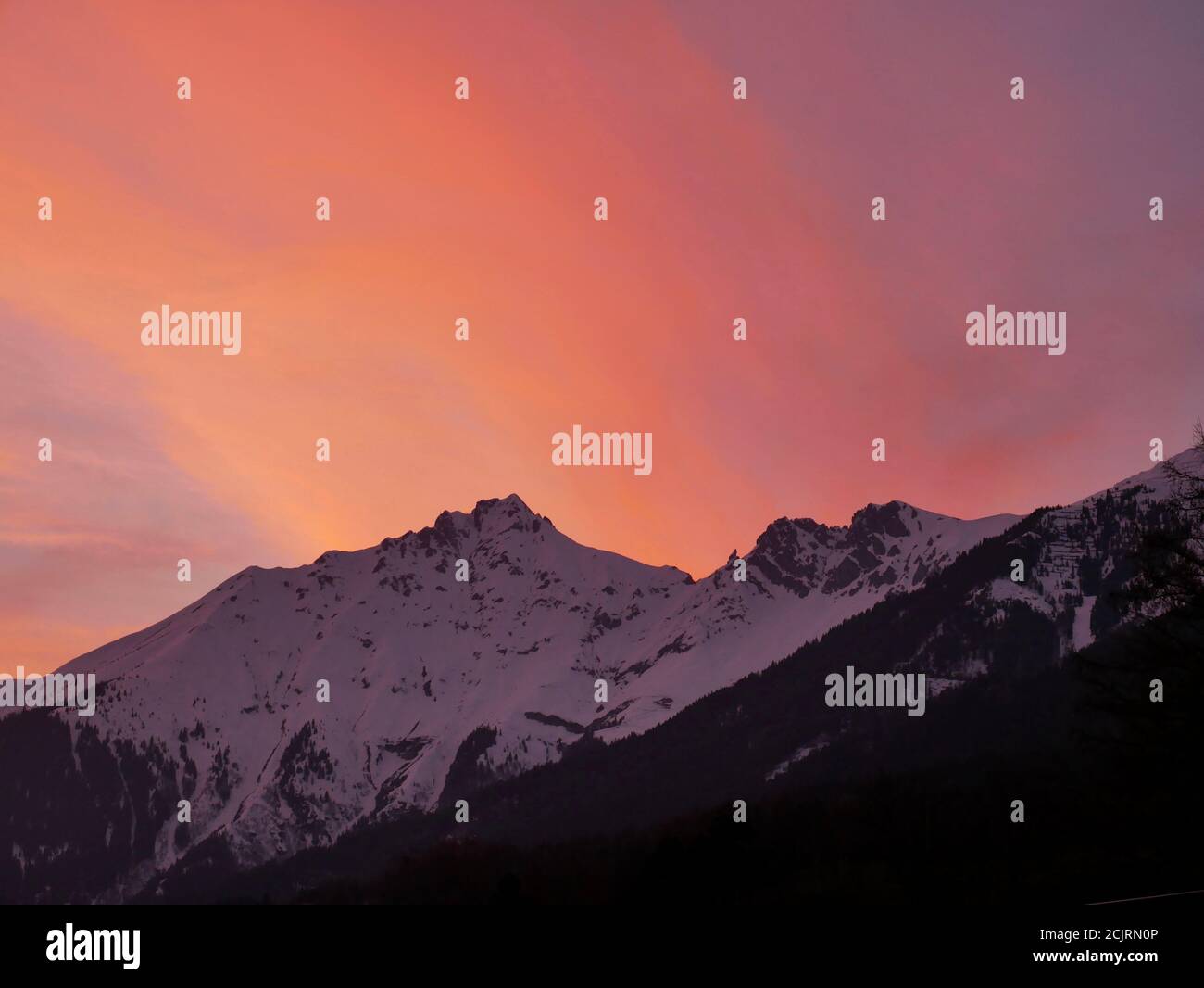 Alpenpanorama vor dem abendroten Himmel. Schneebematte Berge im Abendrot. Banque D'Images