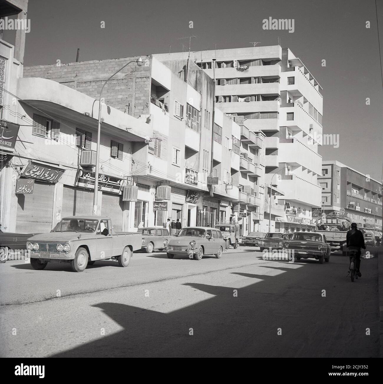 Années 1960, vue de cette époque d'une rue poussiéreuse et semi-tarmaceutique à Djeddah, Arabie Saoudite, montrant des voitures de l'époque et divers bâtiments, plus anciens et modernes. Banque D'Images