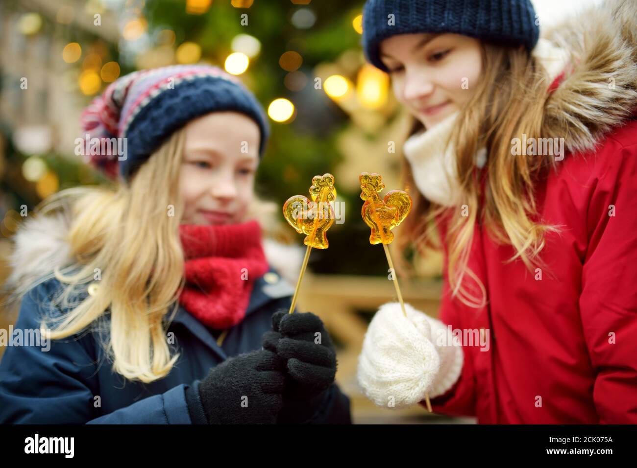 Deux adorables sœurs ayant en forme de coq sur les sucettes de Noël traditionnel à Riga, Lettonie. Les enfants bénéficiant des bonbons, confiseries et pain d'épices Banque D'Images