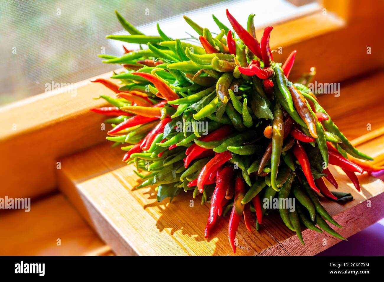Un paquet de piments rouges et verts fraîchement récoltés sur un rebord de fenêtre en bois à la lumière du jour. Fond de nourriture naturelle coloré Banque D'Images