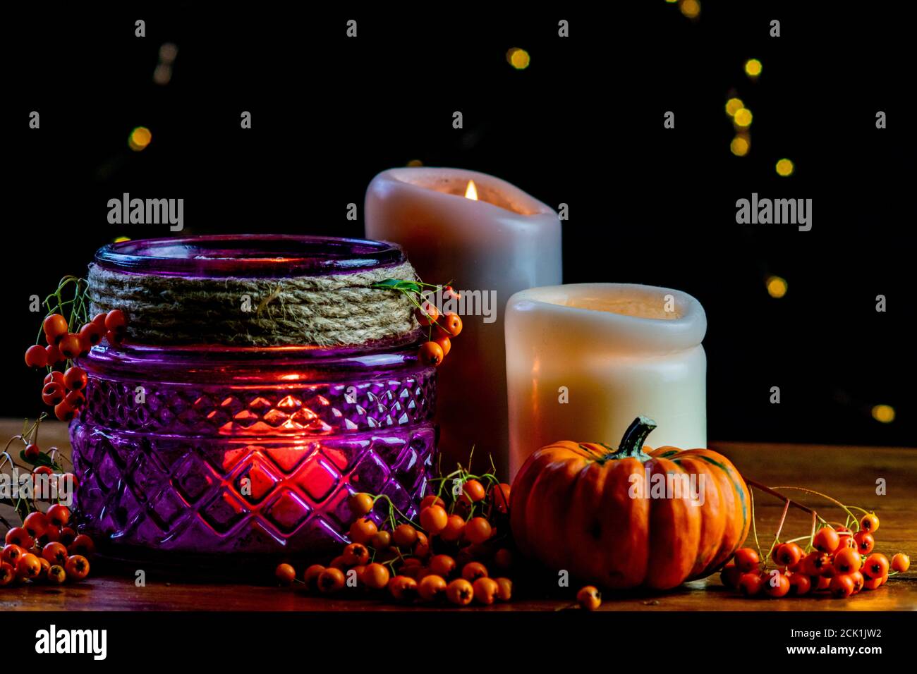 Lanterne violette, citrouille dorée orange baies rowan et deux bougies sur table rustique en bois et fond noir avec points de bokeh jaunes Banque D'Images