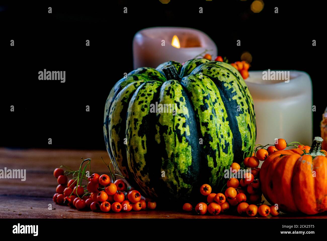 Variété de citrouilles, de baies de rowan et de bougies sur table en bois rustique et fond noir avec bokeh. Automne légumes symboliques en vert, jaune et Banque D'Images