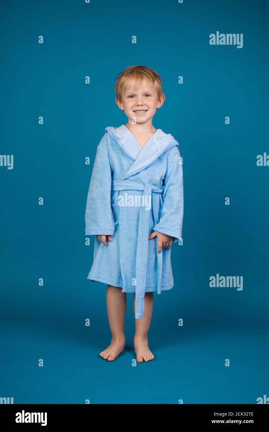 Un joli enfant de 4 ans aux cheveux rouges dans un doux peignoir bleu clair avec une capuche et des cravates est en pleine croissance et regarde l'appareil photo. Studio Banque D'Images