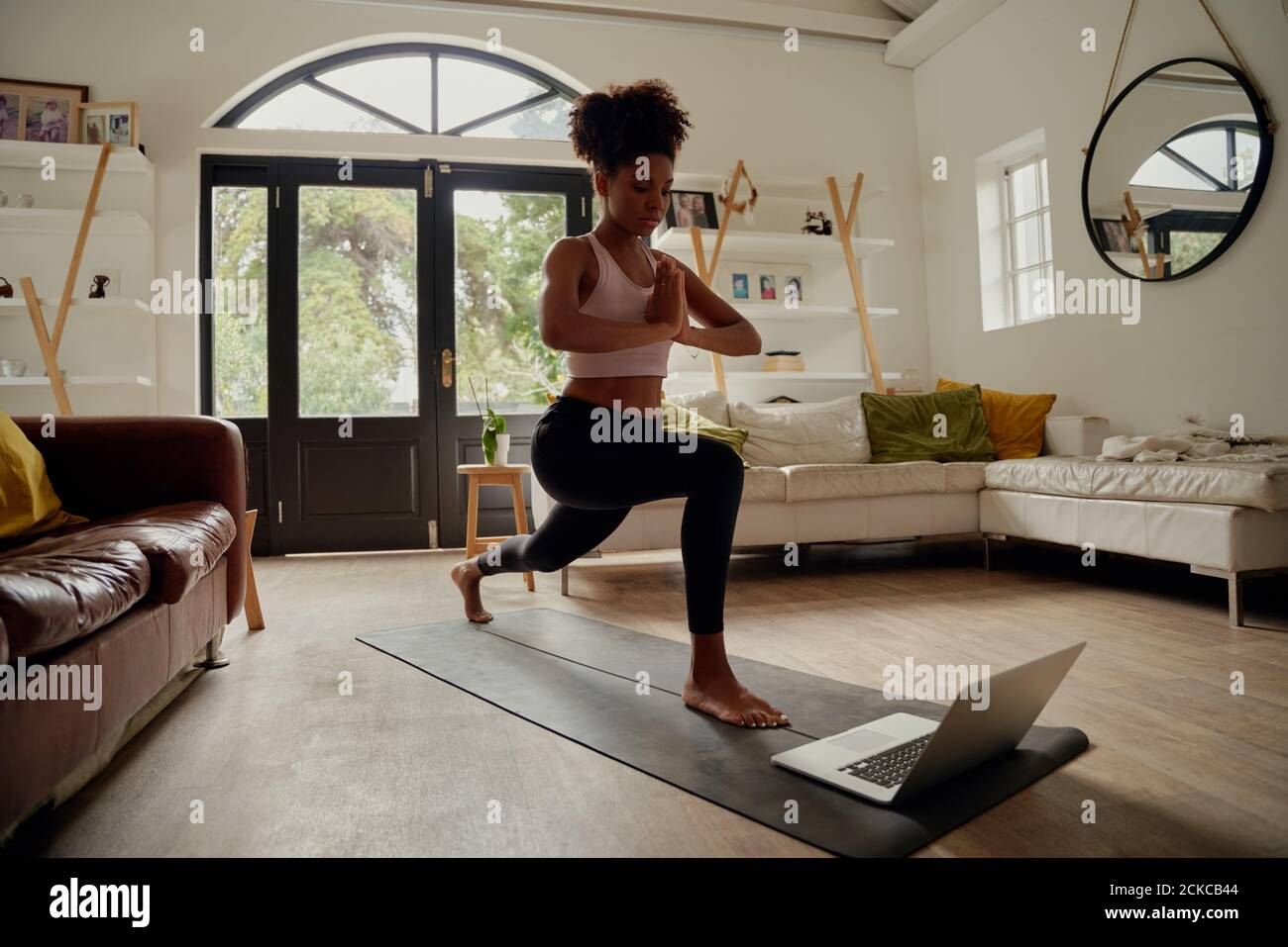 Femme africaine en bonne santé regardant la vidéo sur ordinateur portable tout en faisant de l'exercice avec mains jointes sur le tapis de yoga à la maison Banque D'Images
