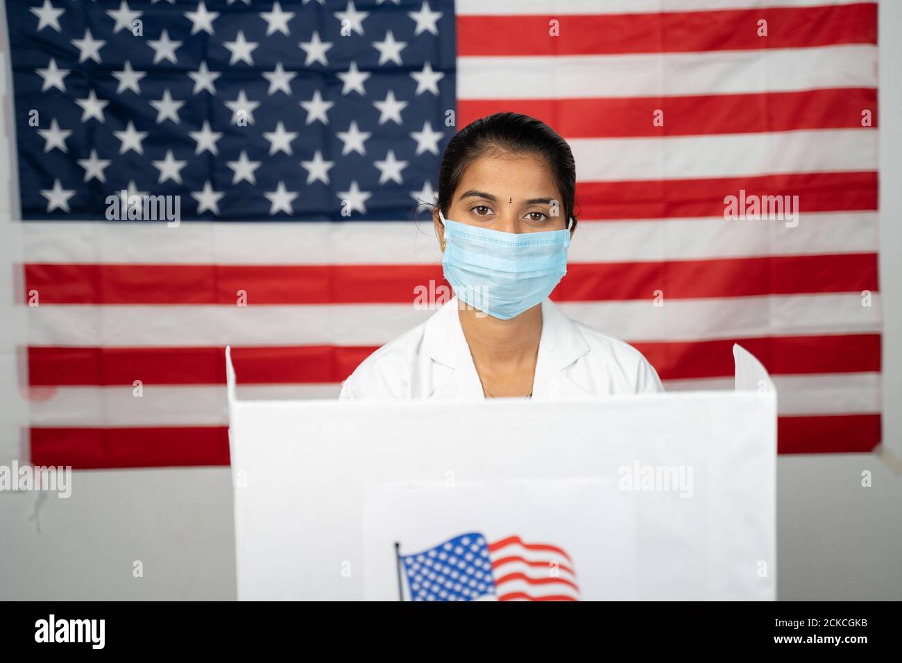 Médecin ou infirmière venant au bureau de vote avec masque médical portant pour le vote - concept de l'élection américaine, en personne votant montrant avec drapeau américain comme Banque D'Images