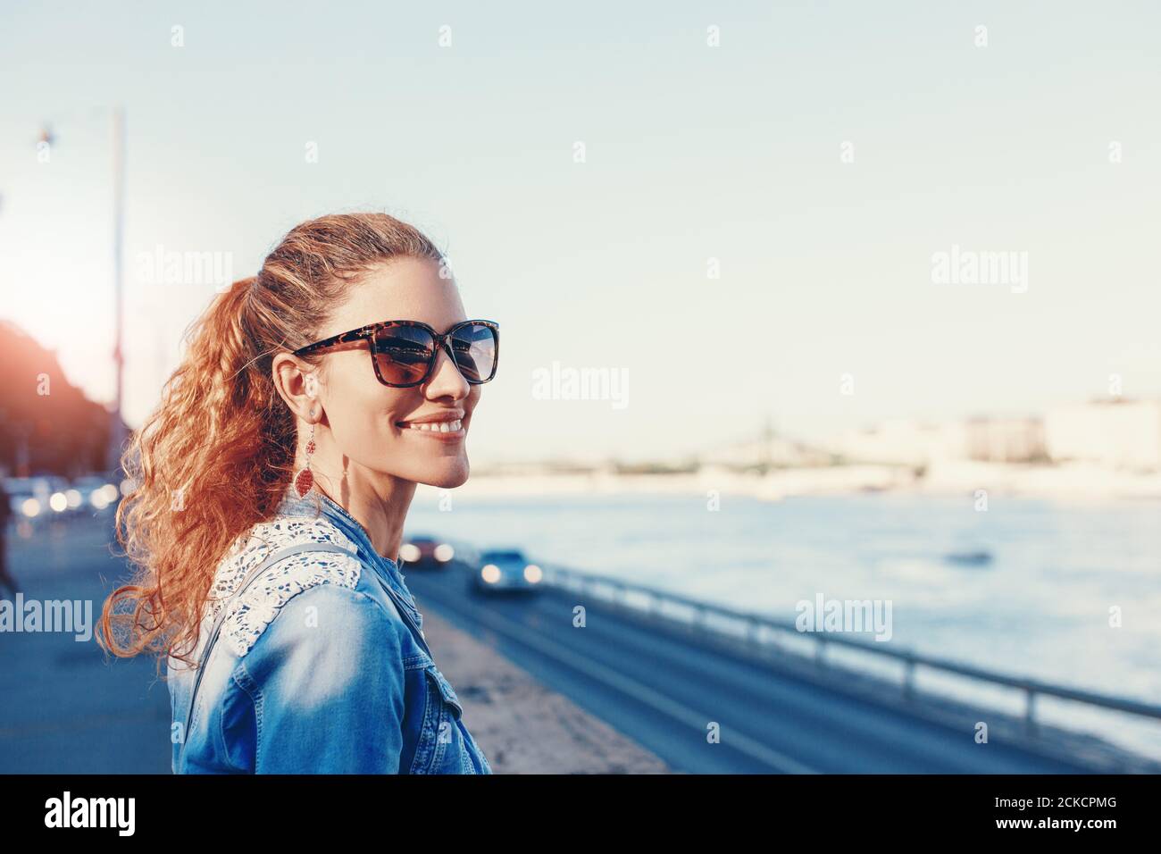 Bonne jeune femme à tête rouge avec un sourire crasseux à la rive de la ville portrait Banque D'Images