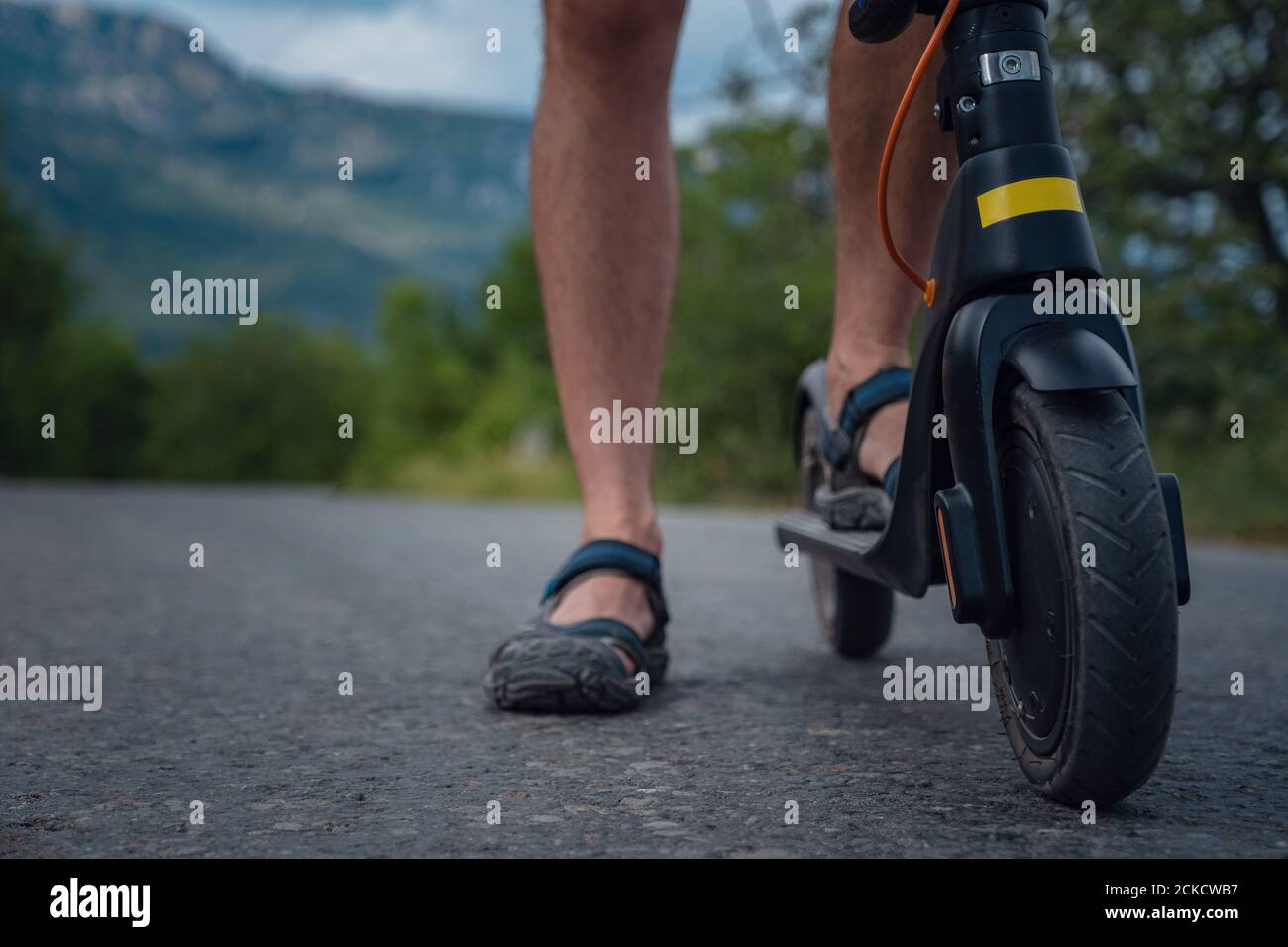 Jeune homme à bord d'un scooter électrique sur la chaîne de montagnes. Gros plan sur un homme qui fait du scooter électrique noir dans un paysage magnifique. Transposor écologique Banque D'Images