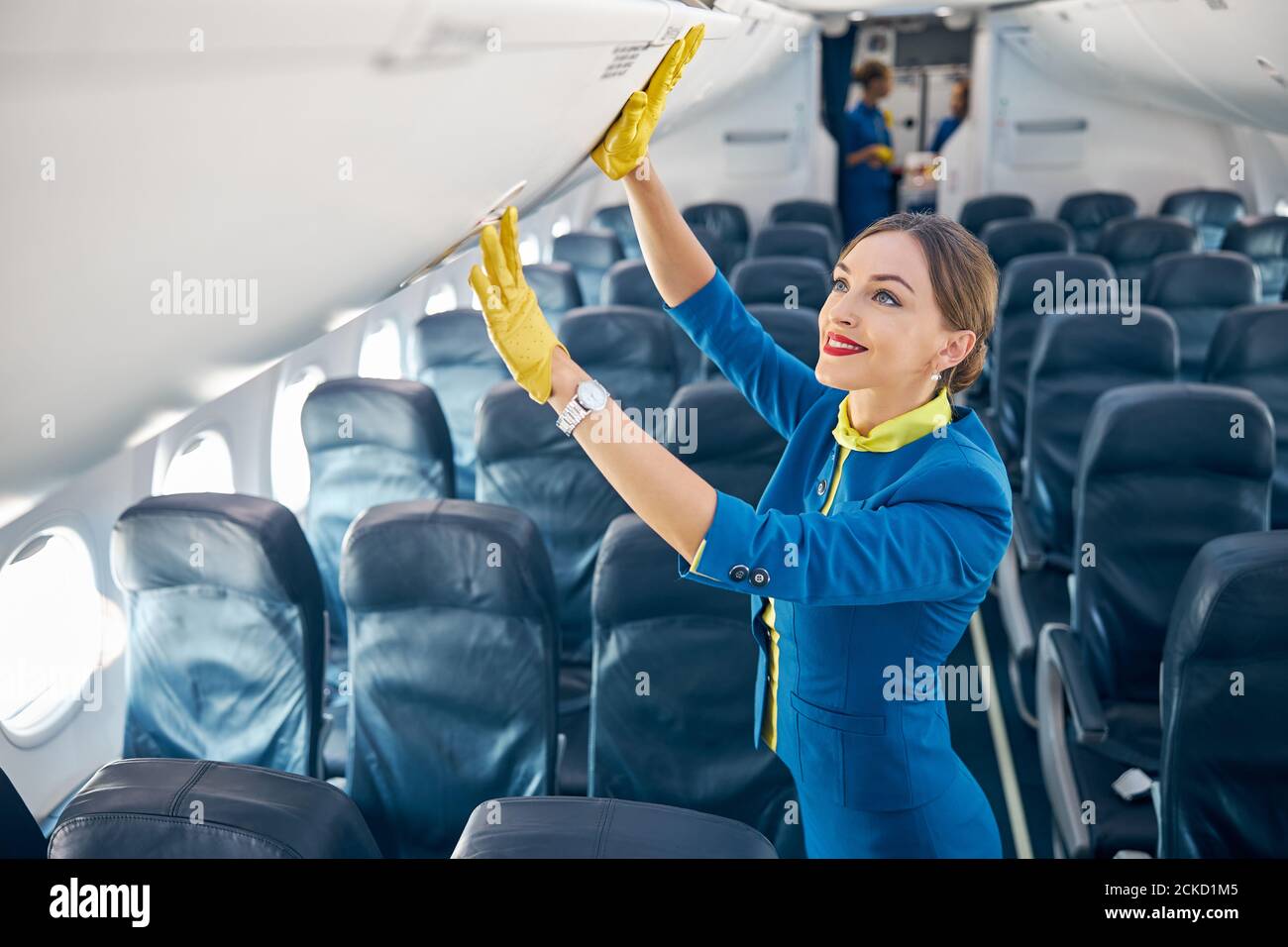 Vérification des gants de costume bleu et de mousseur jaune par le  personnel de bord compartiment avec bagages à main en se tenant dans le  tableau vide d'avion commercial Photo Stock -