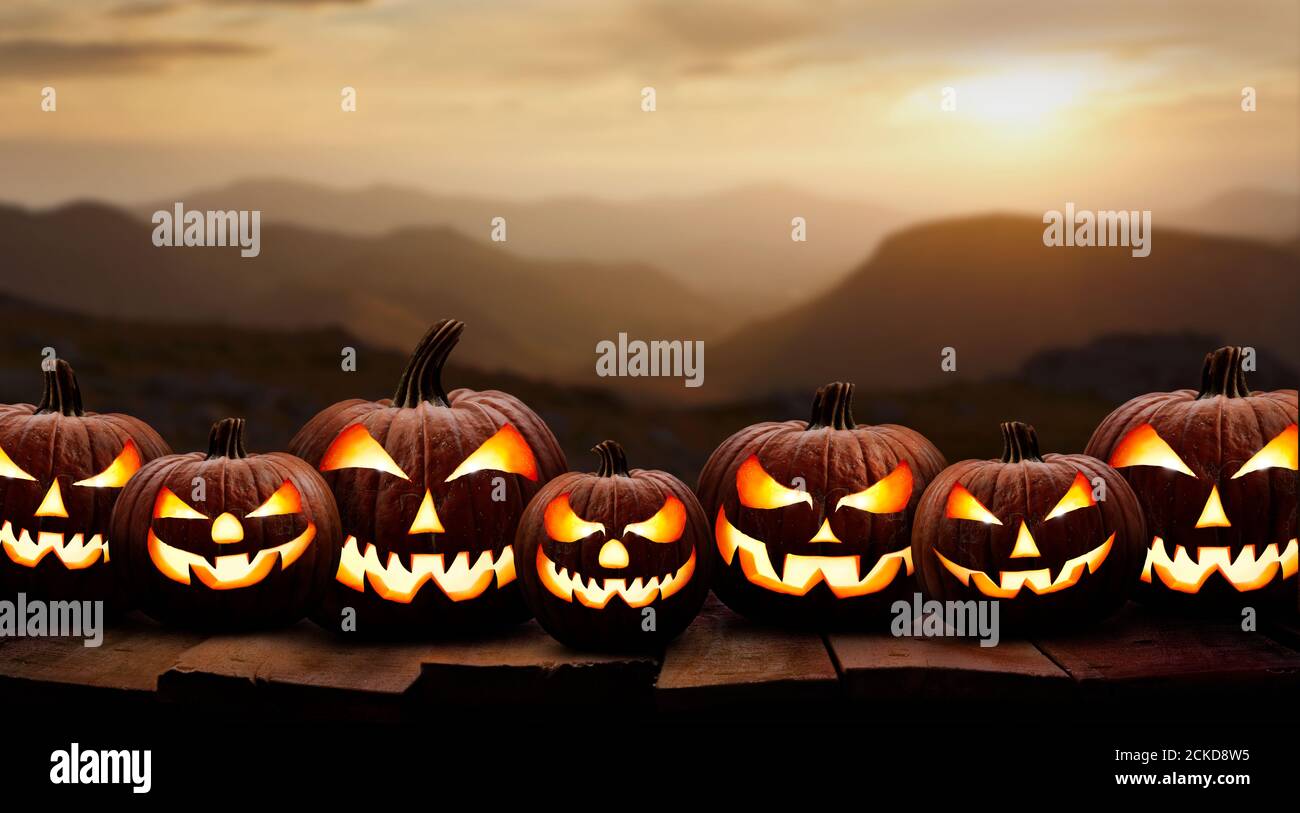 Sept potiron effrayant d'halloween, Jack O Lantern, avec un visage et des yeux mauvais sur un banc en bois, table avec un fond de montagne de coucher de soleil. Banque D'Images