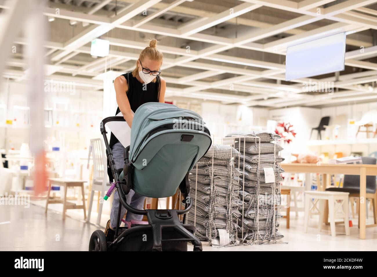 Jeune maman avec nouveau-né dans le magasin de poussettes au détail de meubles et maison accessoires magasin portant un masque médical de protection pour le visage à empêcher l'épandage Banque D'Images
