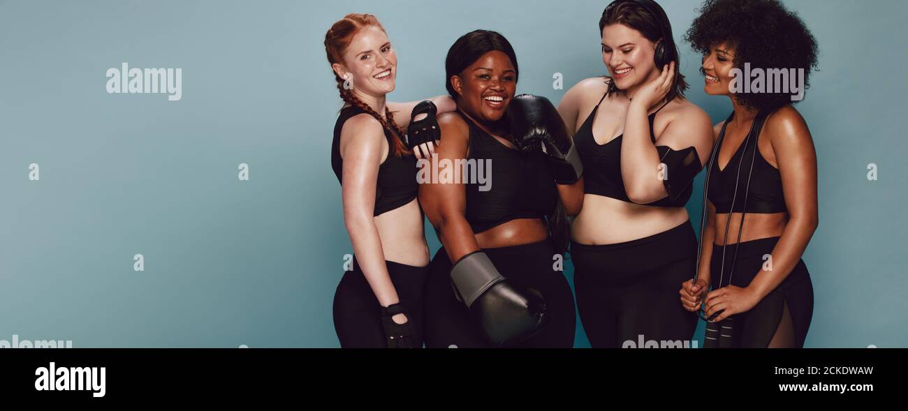 Groupe de femmes de race différente et la taille du corps de l'article vêtements ensemble. Diverses femmes avec des équipements sportifs à la caméra à l'encontre du bac gris Banque D'Images