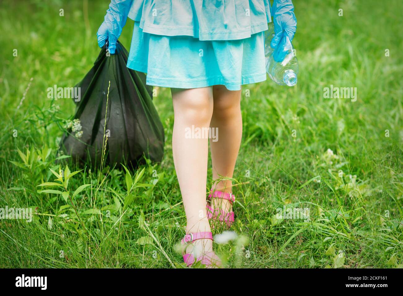 Petite fille avec une bouteille en plastique froissé et un sac poubelle ses mains tout en nettoyant les ordures dans le parc Banque D'Images