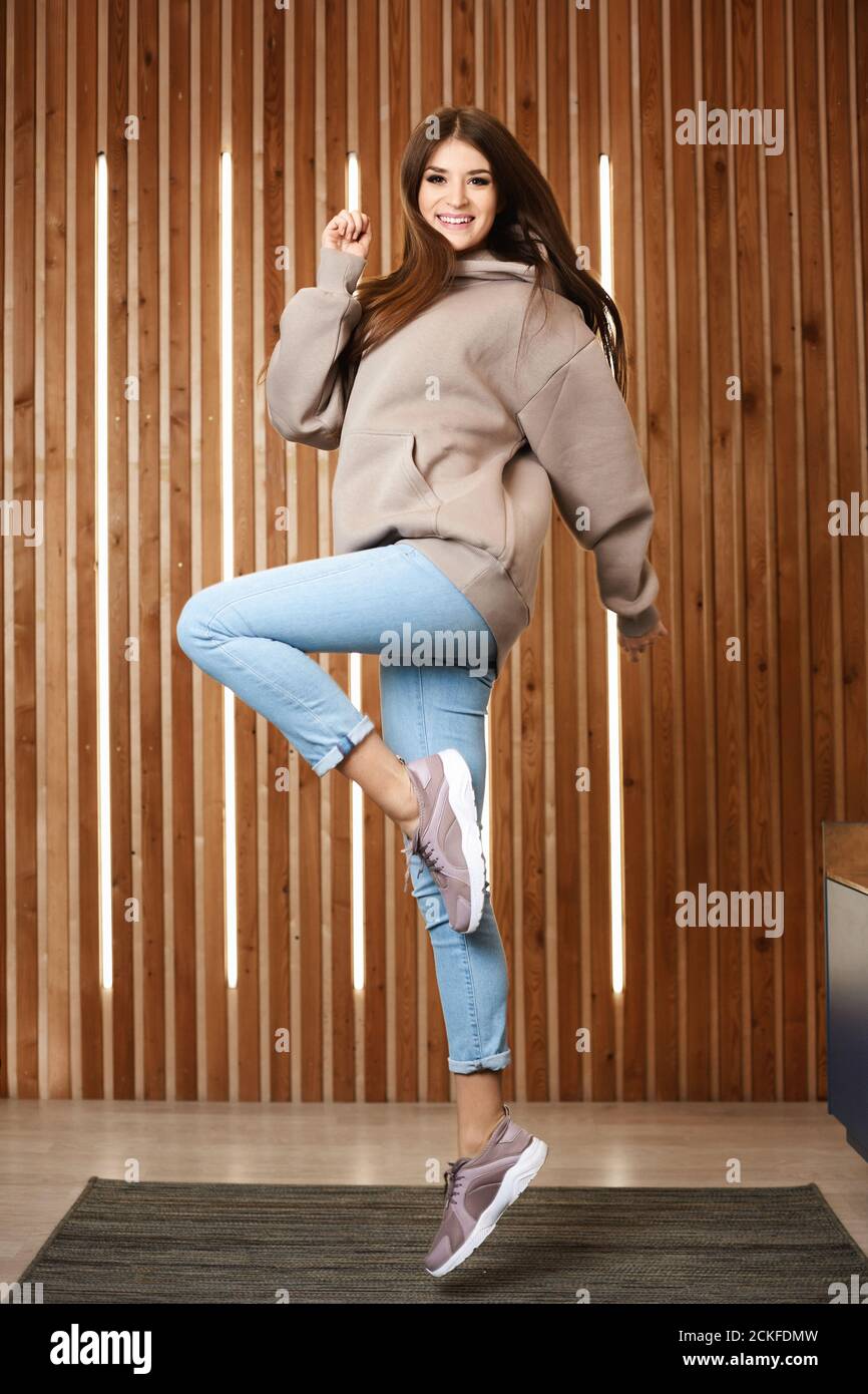 Une jeune fille modèle dans un pull à capuche rose, jeans et baskets bleus  sautant et posant à l'intérieur. Une jeune femme en tenue de sport  décontractée Photo Stock - Alamy
