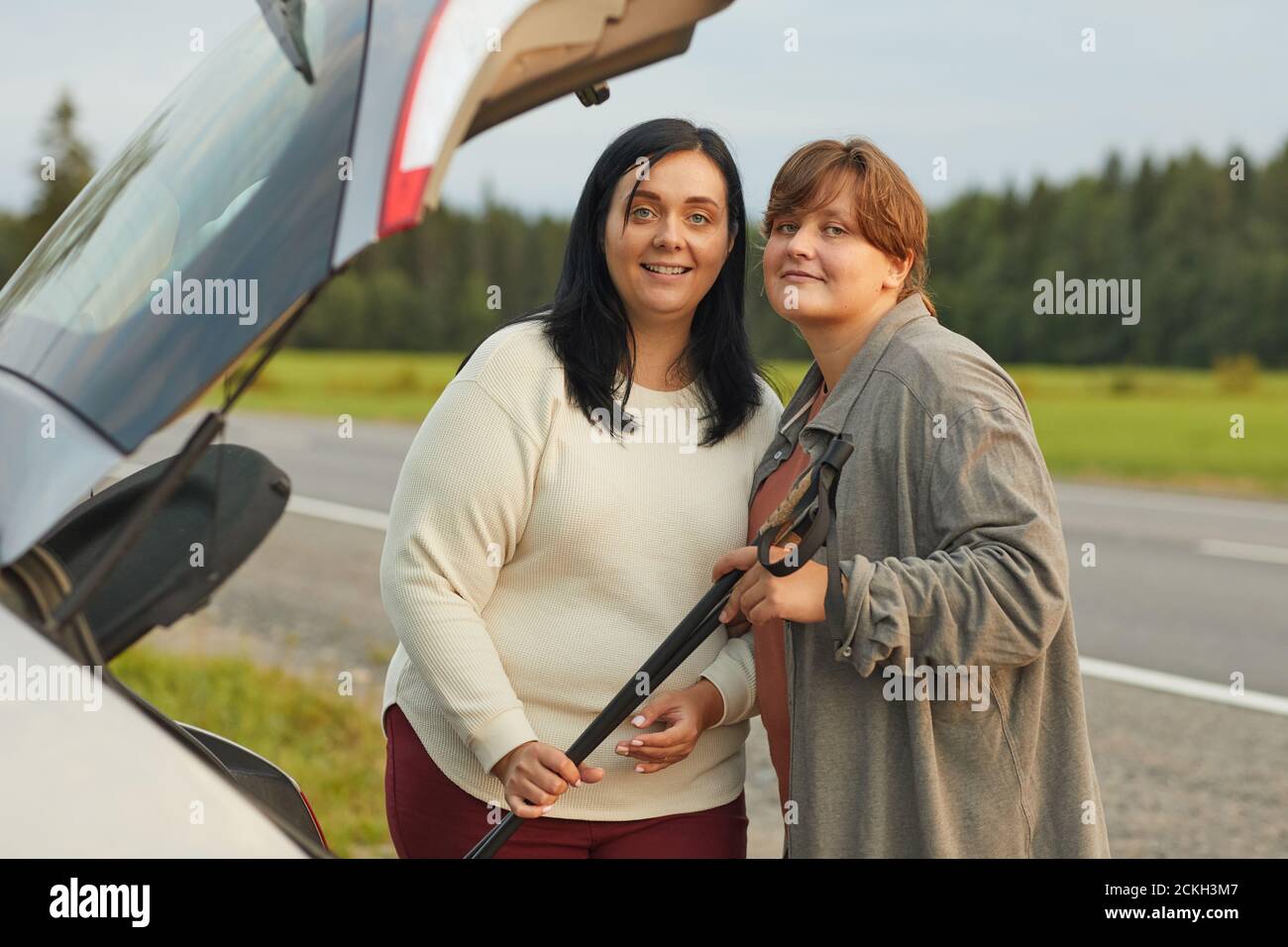 Portrait de deux jeunes femmes debout sur la route et sourire à l'appareil photo en voiture Banque D'Images