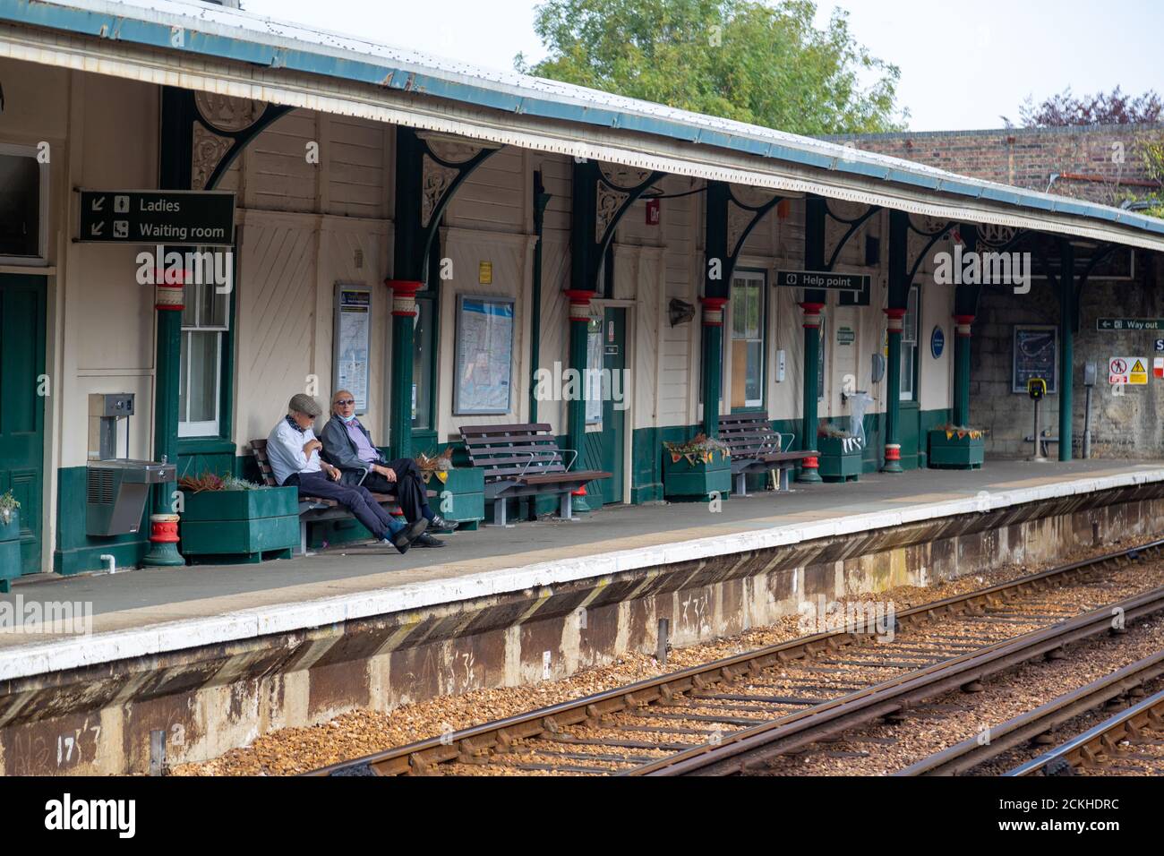 Deux hommes âgés assis sur un banc dans un train station plate-forme en attente d'un train à arriver Banque D'Images