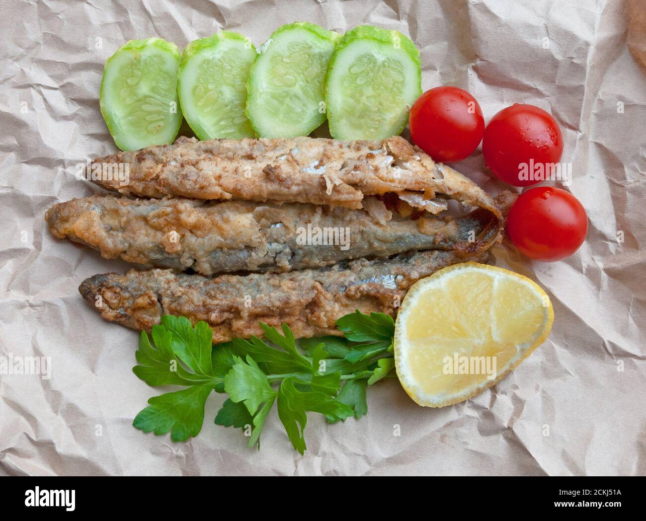 Câline frite avec concombres, tomates cerises, citron et persil sur le papier. Vue de dessus Banque D'Images