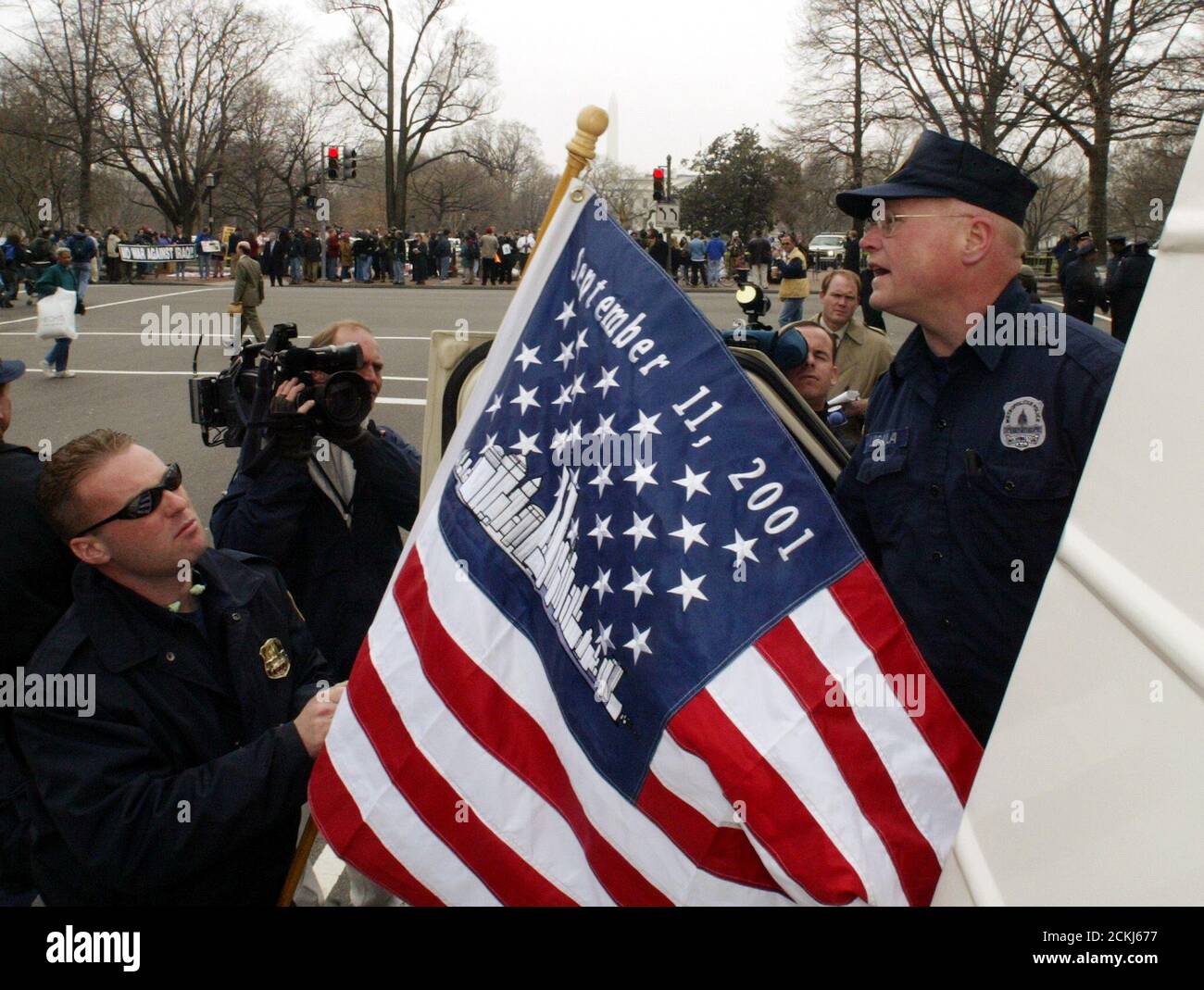Les policiers métropolitains Mark Lewis (L) et James Lugaila (R) ont mis un drapeau des États-Unis orné d'une photo des tours du World Trade Center et du « 11 septembre 2001 » au sommet de leur camion de police lorsqu'ils arrivent pour patrouiller une manifestation anti-guerre près de la Maison Blanche (arrière) à Washington, le 21 mars. 2003. La police a procédé à plusieurs dizaines d'arrestations alors que des manifestants perturbaient la circulation à Washington, tandis que d'importantes frappes aériennes américaines ont frappé le centre-ville de Bagdad en Irak. REUTERS/Jim Bourg JRB/HK Banque D'Images