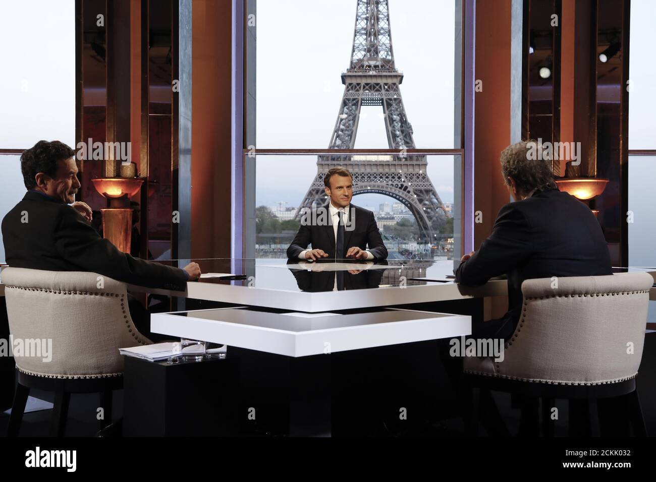 Le président français Emmanuel Macron (C) pose sur le téléviseur avant un  entretien avec le journaliste français du CMR-BFM Jean-Jacques Bourdin (R)  et le site d'enquête de Mediapart le journaliste français Edwy