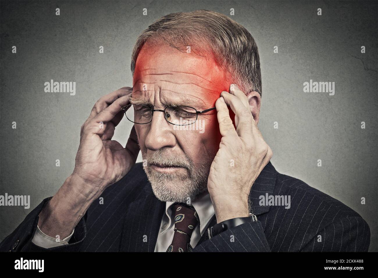 Gros plan tête homme senior souffrant de maux de tête mains sur la tête avec des zones enflammées rouges regardant vers le bas isolées sur fond de mur gris. Humain Banque D'Images