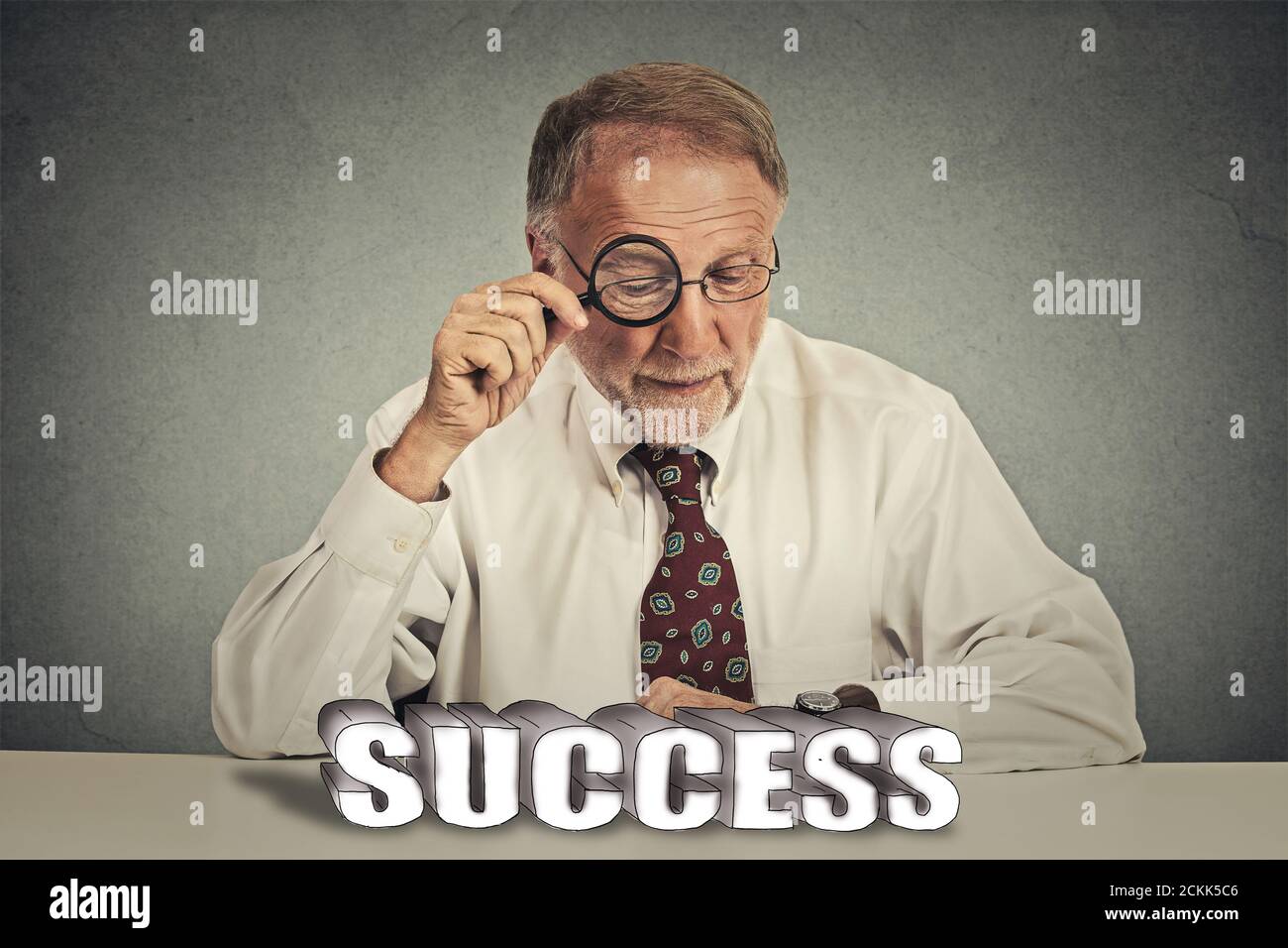 Un homme d'affaires chevronné fait mûrir le patron en costume en regardant à travers la loupe affiche « verre au succès » Banque D'Images