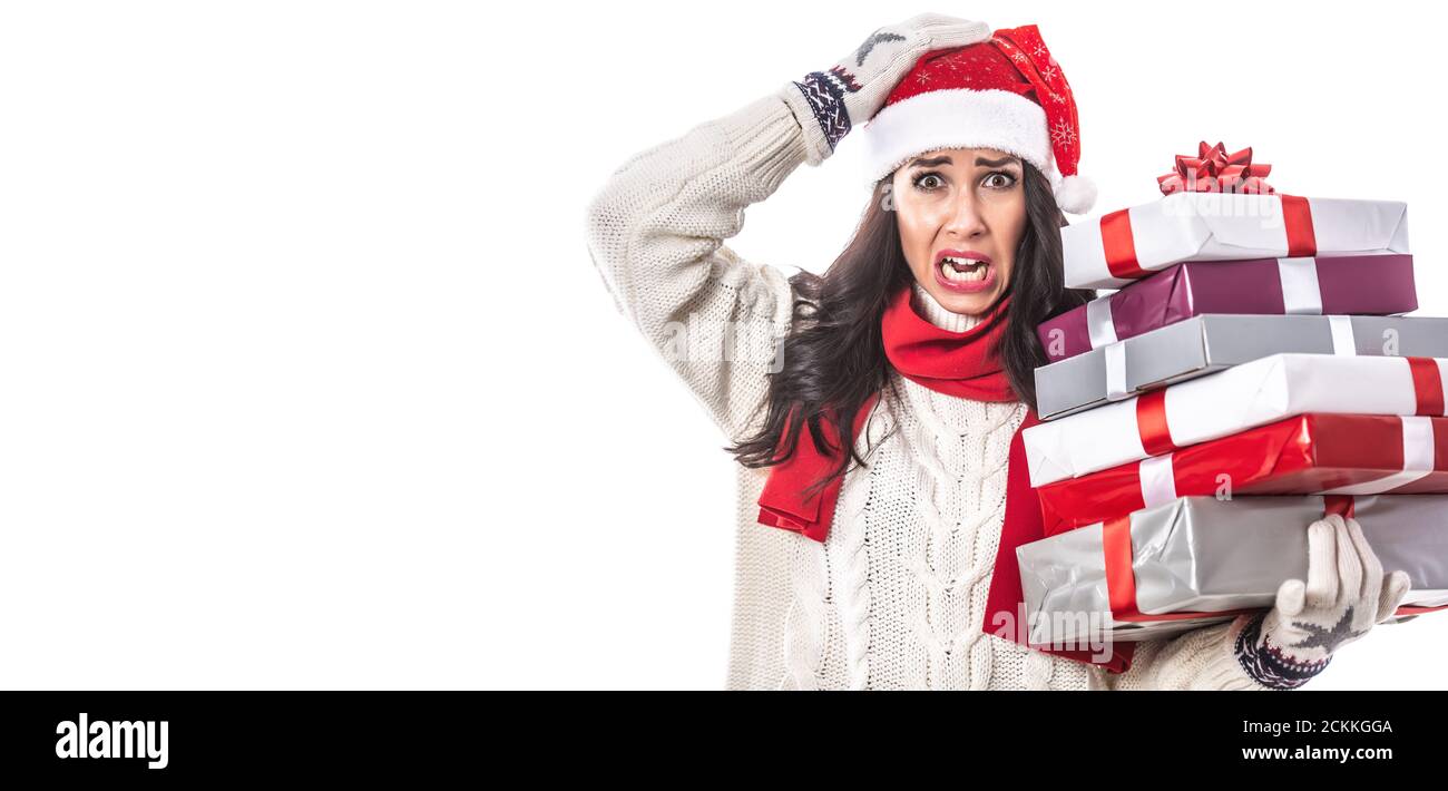 Une femme en casquette de Père Noël et un seater blanc sur fond blanc tient des cadeaux de Noël en train de devenir fou de la ruée saisonnière. Banque D'Images