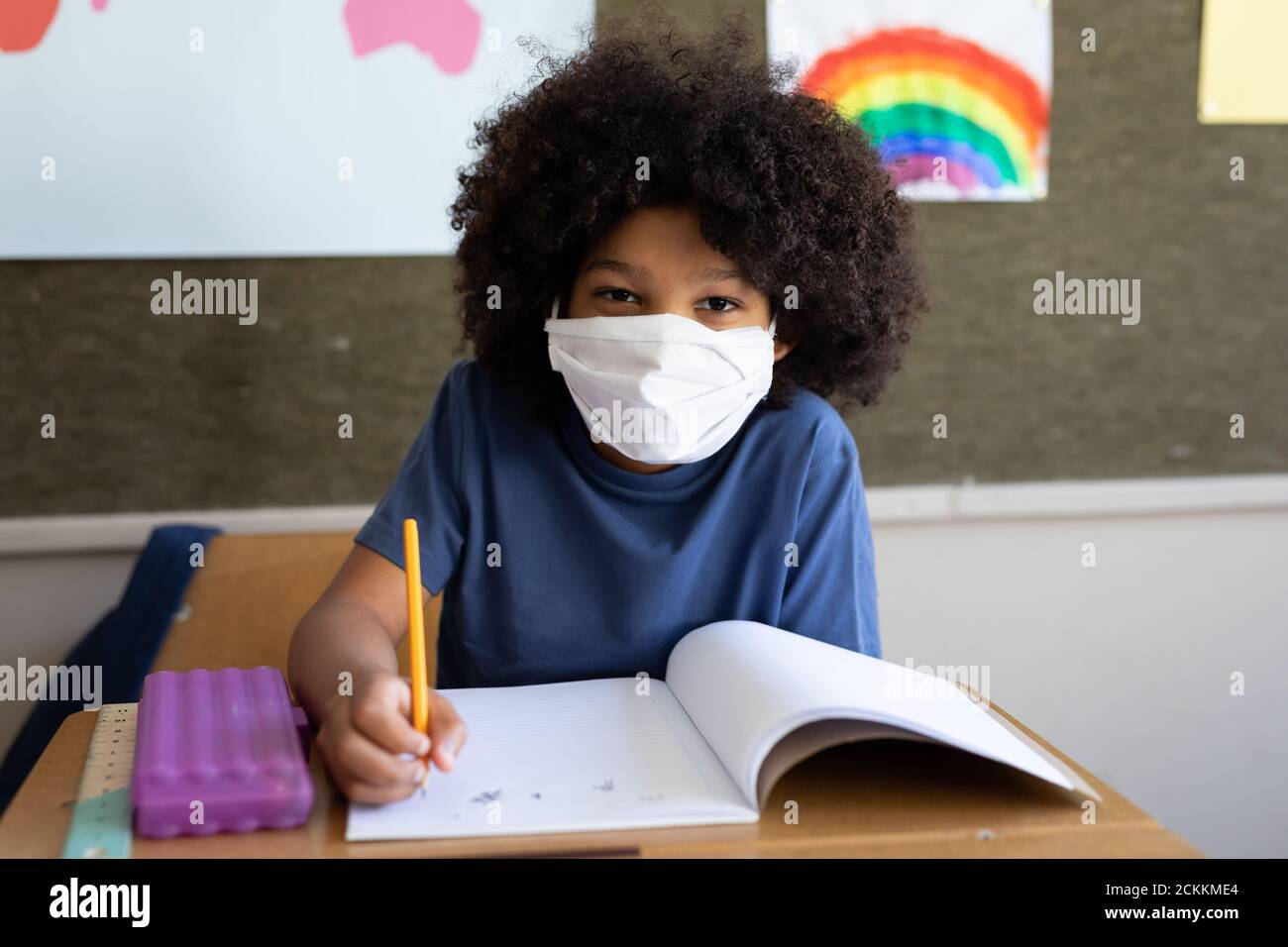 Portrait d'un garçon portant un masque de visage écrit tout en étant assis sur son bureau à l'école Banque D'Images