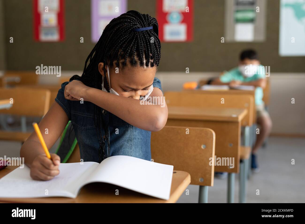 Fille portant un masque facial éternuant assis sur son bureau à l'école Banque D'Images