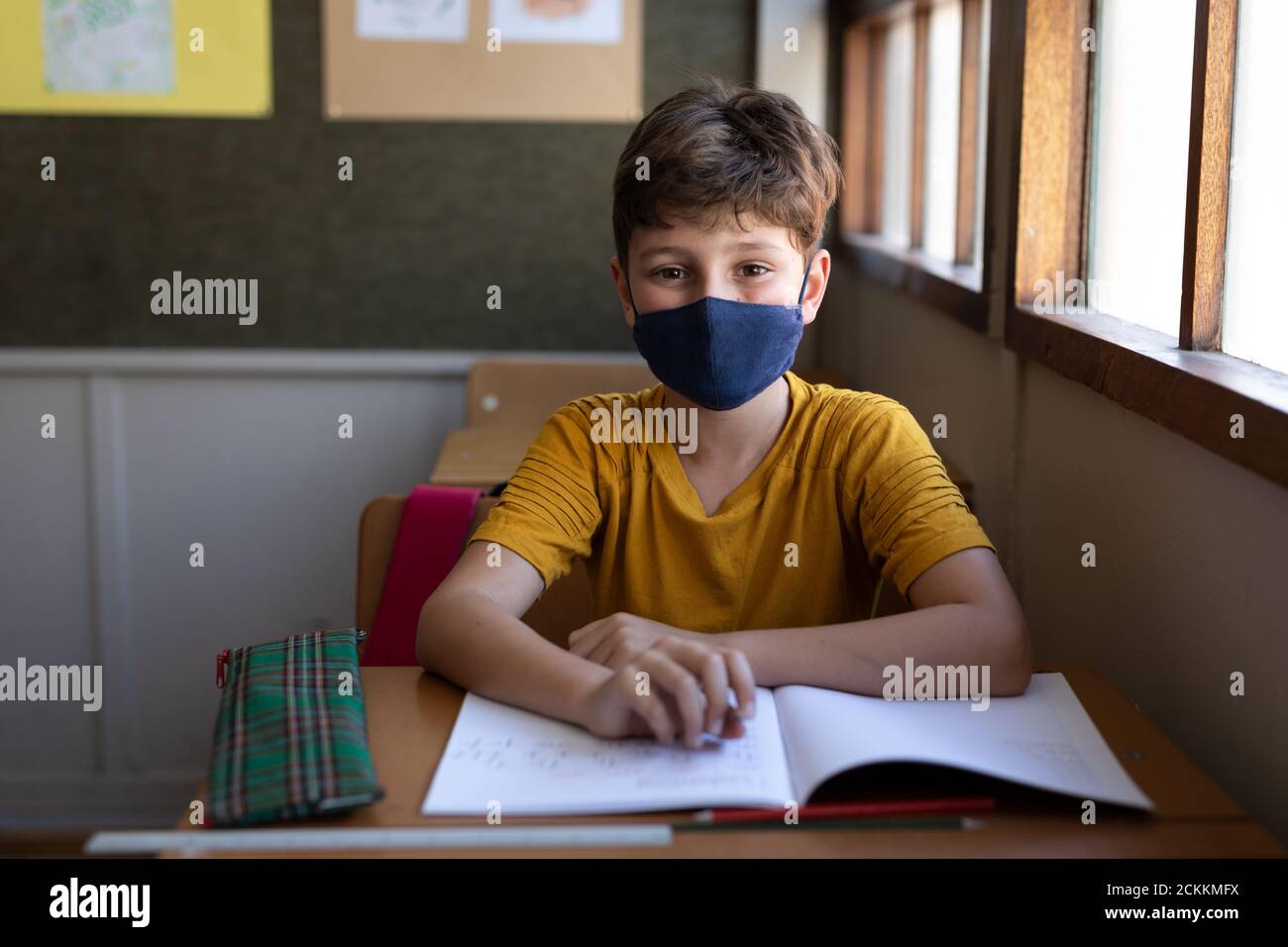 Portrait d'un garçon portant un masque facial assis sur son bureau à l'école Banque D'Images