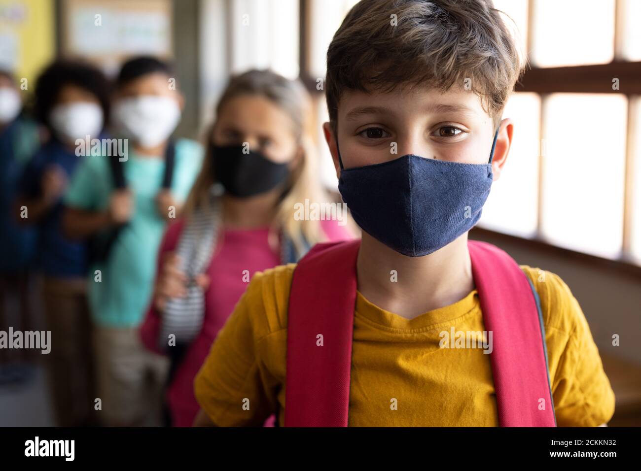 Groupe d'enfants portant des masques avec des sacs debout dans une file d'attente à l'école Banque D'Images