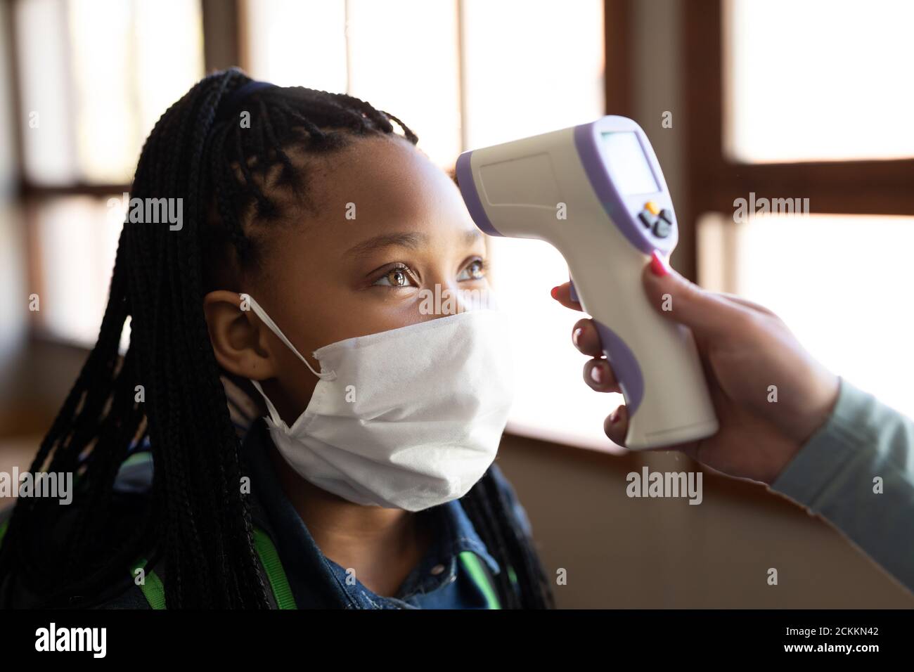 Fille portant un masque facial obtenant sa température mesurée en classe à l'école Banque D'Images