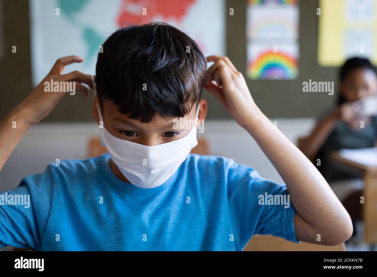 Garçon portant un masque facial assis sur son bureau à école Banque D'Images