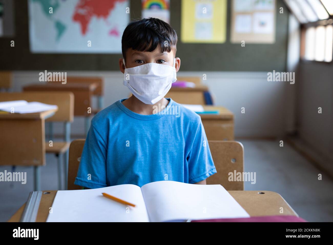 Garçon portant un masque facial assis sur son bureau à l'école Banque D'Images