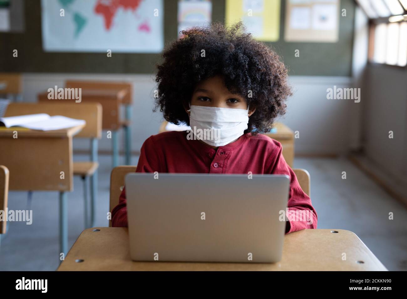 Portrait d'un garçon portant un masque facial avec un ordinateur portable sur son bureau de l'école Banque D'Images