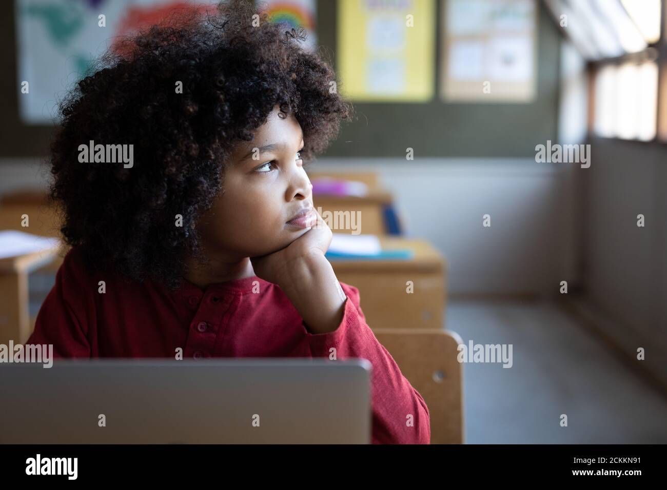 Garçon assis avec un ordinateur portable sur son bureau à l'école Banque D'Images